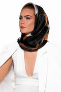Elegant kvinna bär silkescarf som huvudbonad – mönstrad scarf med svart ram och vita, bruna och svarta detaljer.